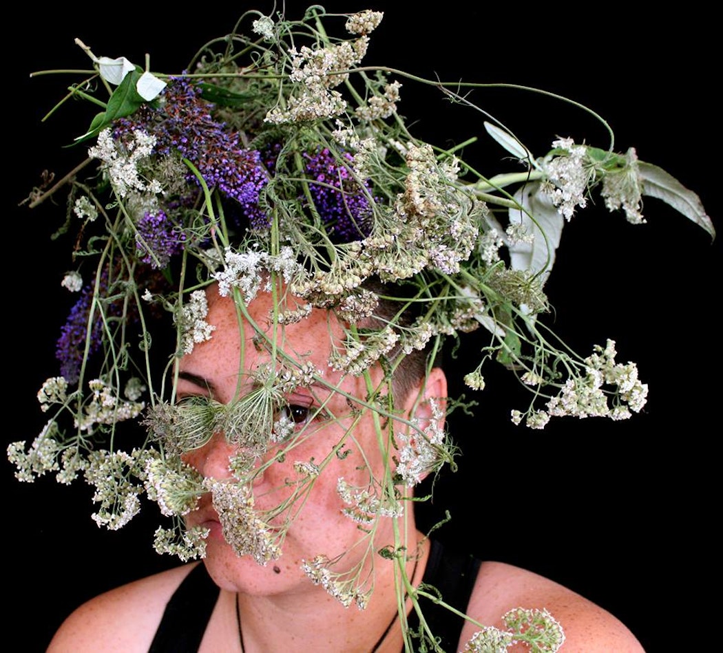 A portrait of Sarah Hudson with their head covered with plants and flowers